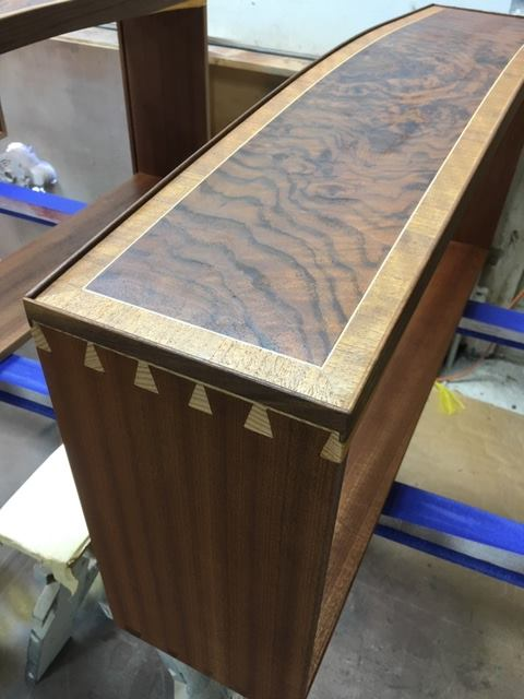 Close-up of a bow-front drawer with a burl walnut veneer center panel, Holly stringing, vertical-grain walnut surround, solid walnut bead edge, and hand-cut dovetails on a mahogany drawer box.