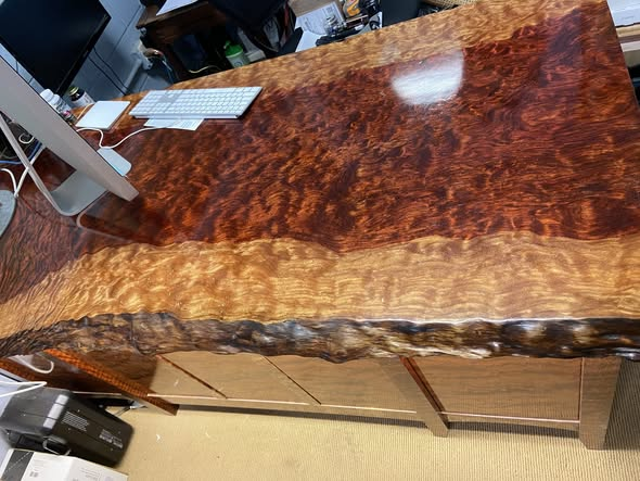 Wider view of the bubinga desk from the keyboard side, showing the full 72-inch top, dramatic burl figure, and bubinga storage piece tucked beneath.