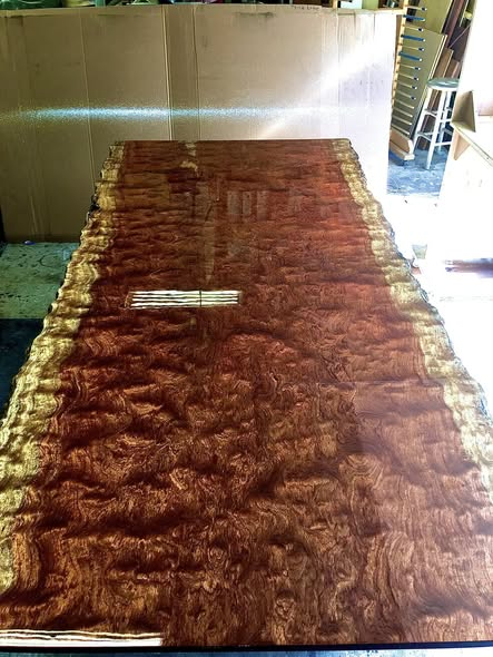 Large bubinga table top with dramatic figured grain, live edges, and a mirror-like high-gloss finish reflecting overhead shop lights.