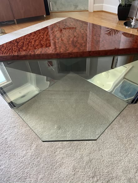 Pentagonal bubinga coffee table with mirror-gloss finish on a beveled glass base, installed in a living room.
