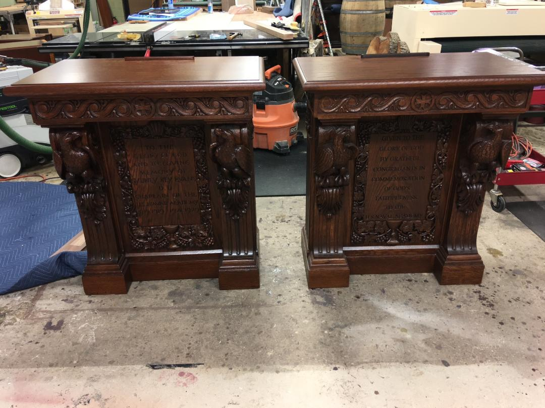 A pair of matching hand-carved quartersawn white oak lecterns with carved eagles, acanthus leaves, scroll detailing, and inset engraved panels reading 'Given to the Glory of God... US Naval Academy', finished in a warm reddish-brown stain.