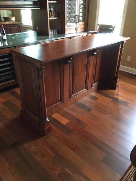 Custom cherry home bar with raised panel doors, turned columns, and a parquet-pattern solid cherry top finished in a warm dye, stain, and glaze combination over Brazilian cherry flooring.
