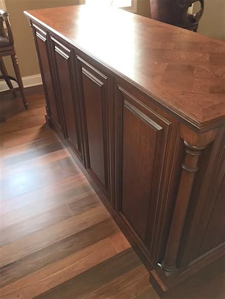 Angled view of the cherry home bar showing the parquet top edge, raised panel doors with applied moldings, and turned column corner.