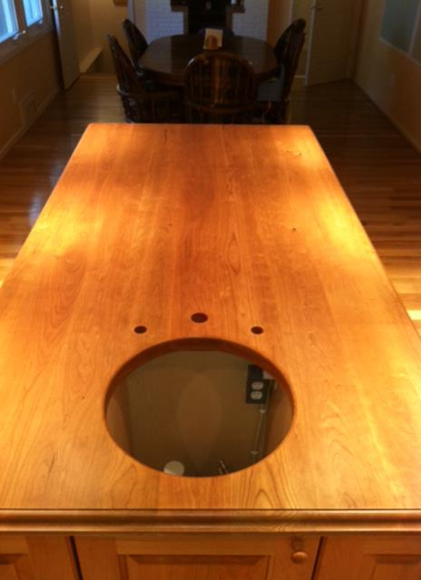 Solid cherry kitchen island top with cooktop cutout and three pre-drilled faucet holes, bullnose edge, and warm hand-rubbed finish