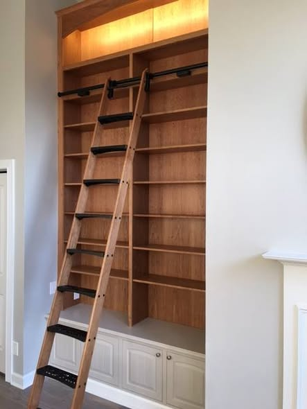 Custom 12-foot cherry bookcase with rolling library ladder, fixed dado shelves, painted base cabinet, and a dimmable LED light glowing in the upper arched cabinet.
