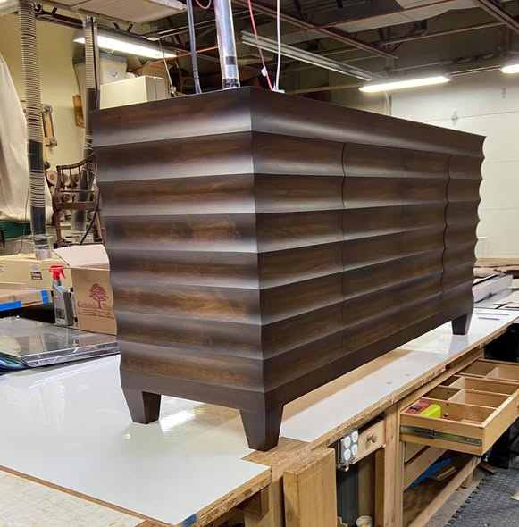 Hard maple dresser with horizontal cove-cut ribbed front and sides, tapered feet, finished in a bright amber dye under an espresso stain, photographed on the workbench in the shop.