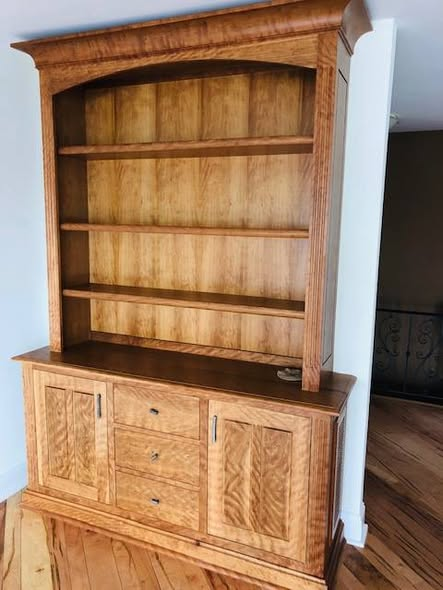 Natural curly cherry hutch with arched crown, three open upper shelves, two raised-panel lower doors flanking three center drawers, showing dramatic curly figure across every panel.