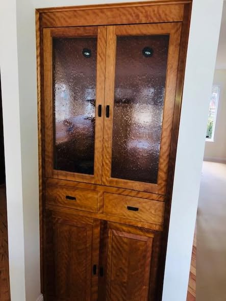 Tall curly cherry built-in cabinet with seeded glass upper doors, two small drawers, and lower raised-panel doors, highlighting the wavy curly figure of the natural cherry.