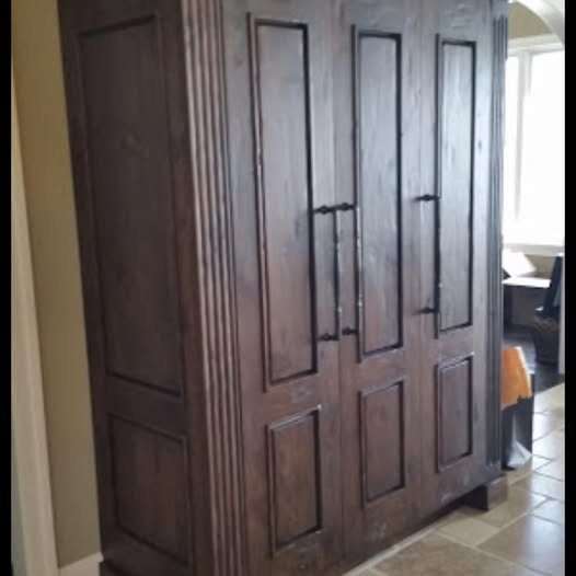 Handmade refrigerator surround cabinet with hand-scraped dark-stained wood, raised-panel doors, fluted side pilaster, and turned center pull