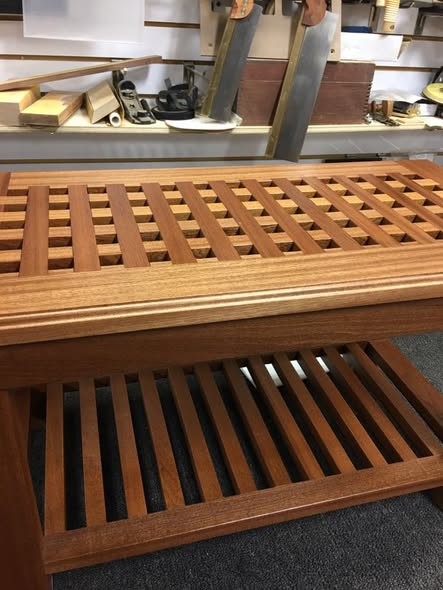 Side view of the mahogany lattice table in the shop showing the deep half-lap grid pattern of the top and the slatted lower shelf below.