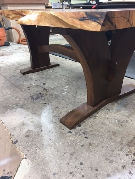 Side view of the Matumi slab resting on a custom walnut trestle base with arched stretcher and curved supports.