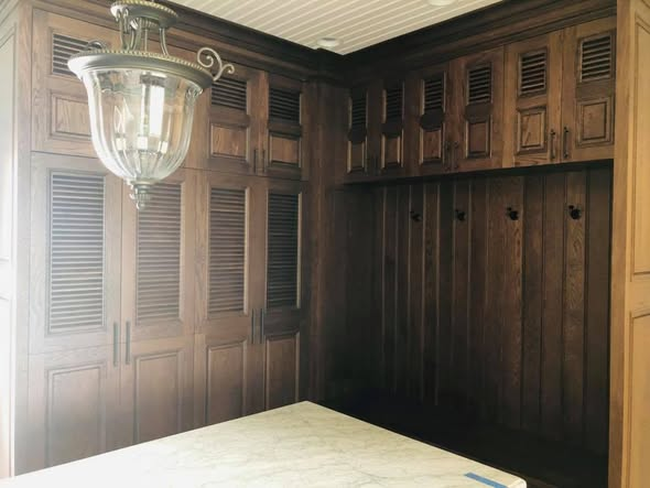 Corner view of the white oak mudroom showing louvered cabinet doors wrapping around with a built-in bench seat and coat hooks along the back wall.