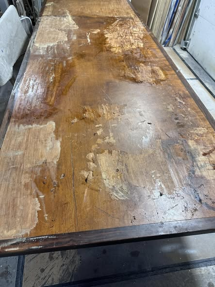 A 12-foot long historic Nara table from the Naval Academy during restoration, with thick shellac being scraped from the wide single-board top bordered by Philippine ebony.