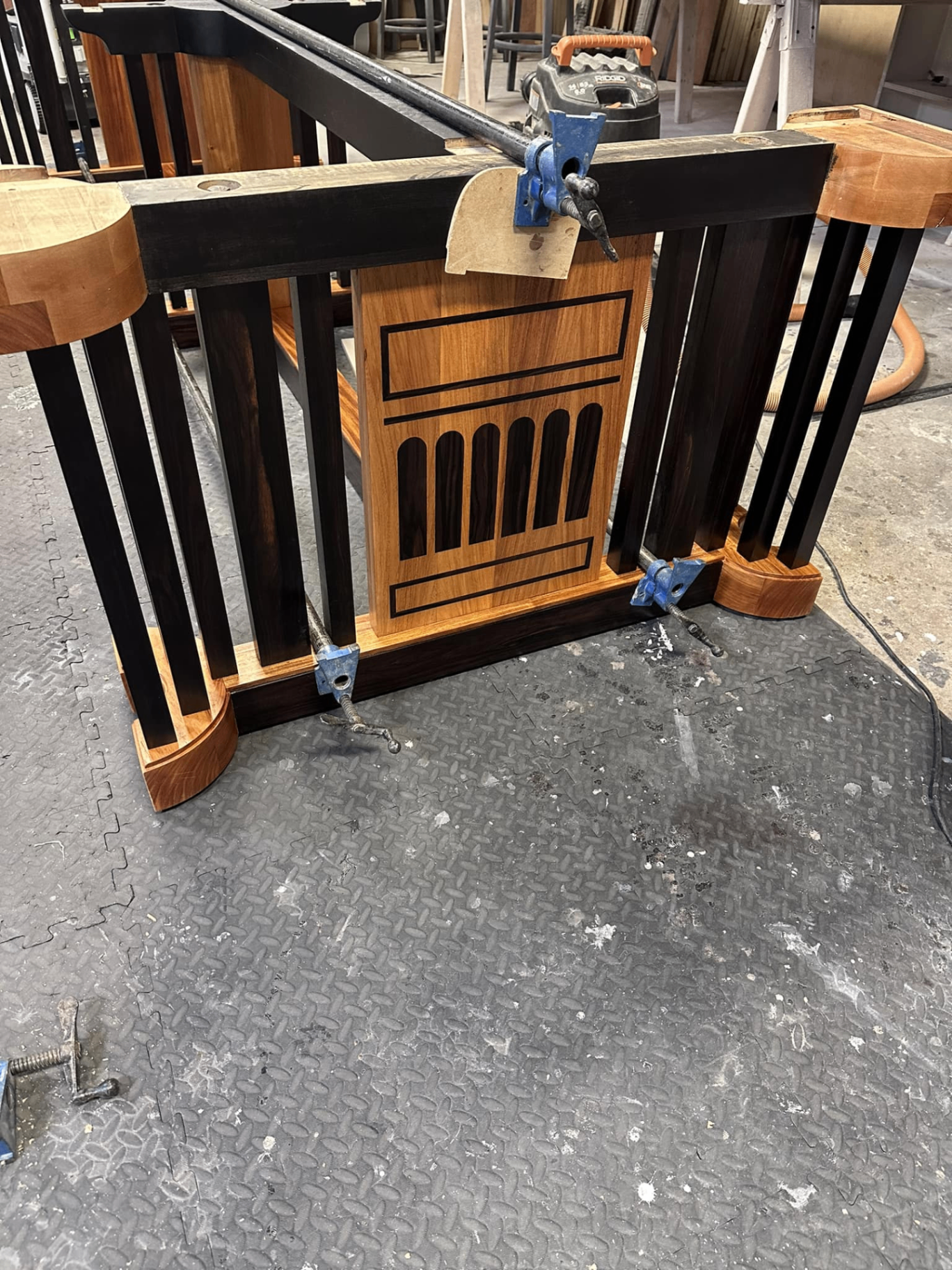 Close view of the restored inlay panel and dark slatted base detail on the Naval Academy table, clamped in the shop during repair and refinishing work.