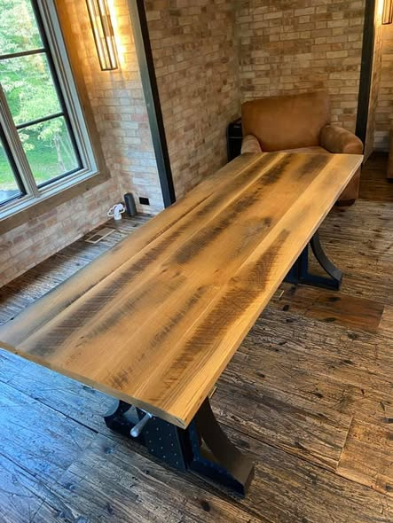 Angled view of the reclaimed white oak desk showing long board grain, weathered patina, and dark mineral streaks, with the cast-iron crank base partially visible beneath.