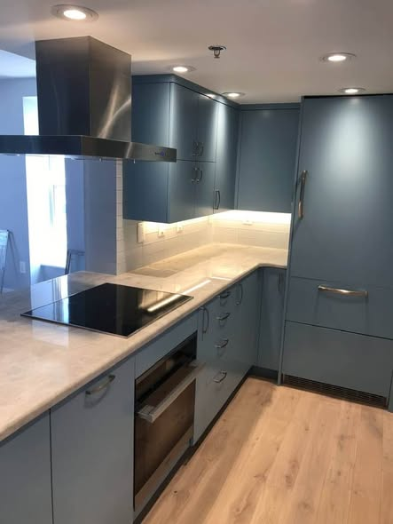 Slab-front blue-gray kitchen on Pennsylvania Avenue DC with stainless island hood, induction cooktop, integrated panel-front refrigerator, white subway tile backsplash, and pale wood floor