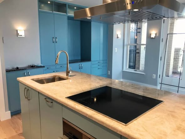 Island and perimeter view of the Penn Ave kitchen showing quartzite waterfall counters, undermount sink with brass faucet, stainless island hood, sconces, and tall blue cabinets