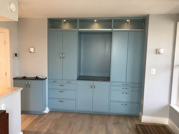 Floor-to-ceiling blue cabinetry wall with center display niche, lit glass uppers, stone counter, and stacks of flat drawers below