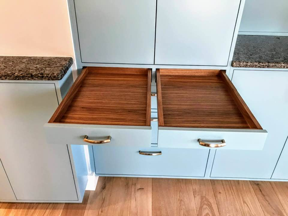 Two open walnut drawers side by side in the Penn Ave kitchen with brass bow pulls and matching wood floor below