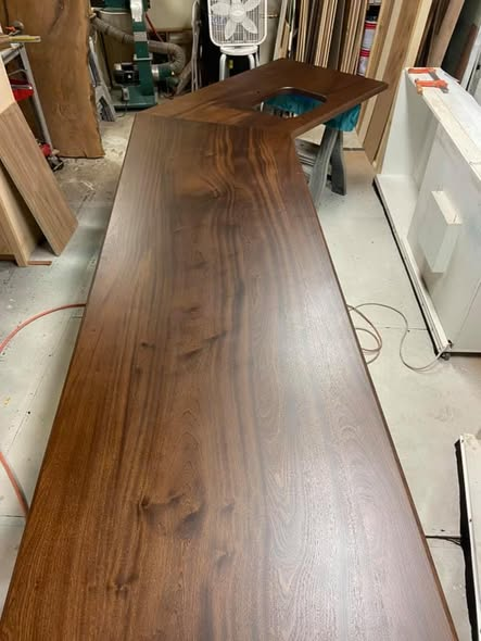 15-foot long Sapele mahogany kitchen island top with a custom warm brown stain and low-sheen isocyanate urethane finish, shown in the shop with an undermount sink cutout.