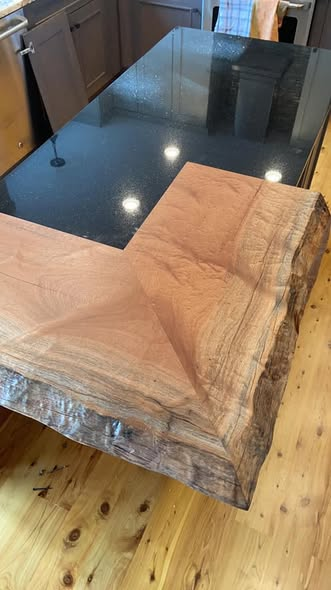 Figured Sapele mahogany kitchen island top with a waterfall end cascading over a black granite surface, showing live edge detail and rich ribbon grain finished in low-sheen isocyanate urethane.