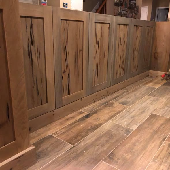 Sinker cypress kitchen island in progress — pecky cypress door panels in clear cypress frames, finished with a custom dye-and-stain combination matched to the wood-look tile floor