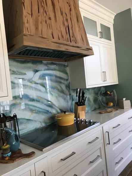Close-up of the pecky cypress range hood above a cooktop with a hand-poured fused glass backsplash in greens, blues, and yellows.