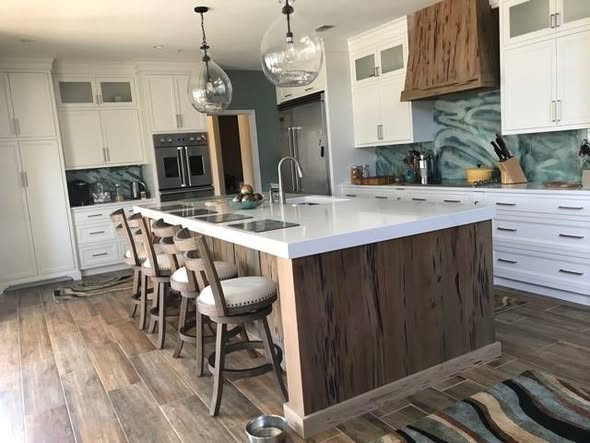 Custom kitchen with a large sinker cypress island and matching pecky cypress range hood, white perimeter cabinets, glass pendant lights, and a swirling green glass backsplash.