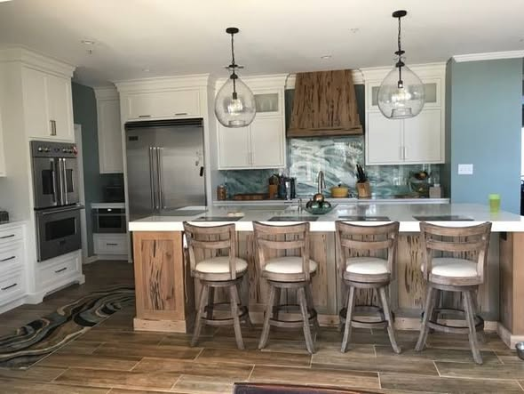 Front view of the sinker cypress kitchen island with four bar stools, pendant lights overhead, and the pecky cypress range hood on the back wall.