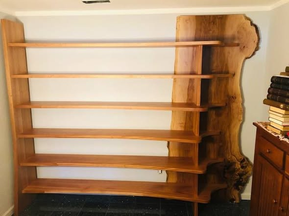 A 96-inch wide, 85-inch tall bookcase with live edge sycamore slab sides supporting six African mahogany shelves set into dadoes across the face of the sycamore.