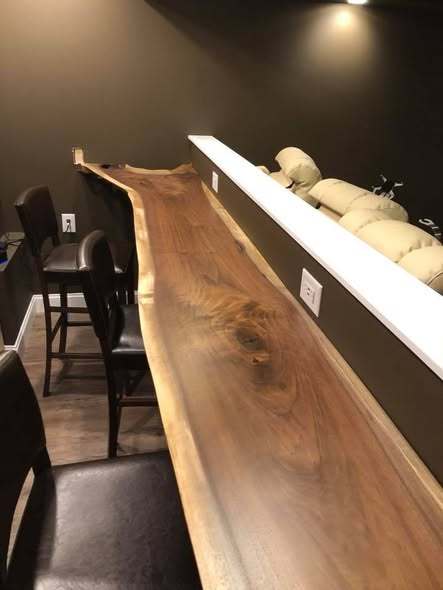Long view of the live-edge walnut bar top running along a home theater wall with bar stools pulled up and theater recliners visible beyond.
