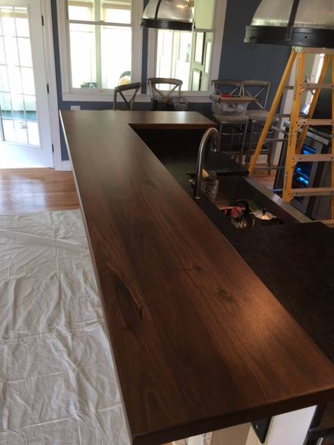 Long bar-height walnut kitchen counter top installed against a navy wall, with a deep rich finish, integrated sink cutout, and seamless floating edge with no visible brackets