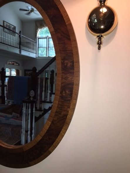 Detail of the oval burl walnut mirror with vertical-grain walnut banding around the frame, reflecting a staircase and arched window.