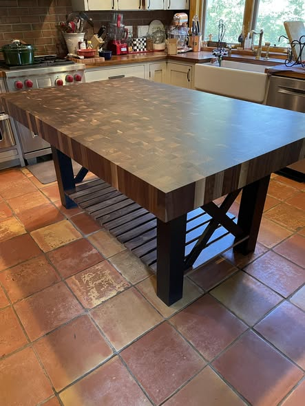 Walnut end-grain butcher-block kitchen island with thick checkerboard top and black X-frame base on saltillo tile floor