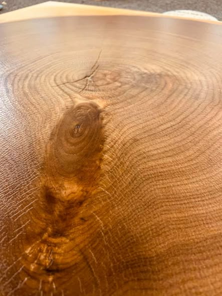 Close-up of the walnut cross-section veneer showing the growth rings, sapwood, and a knot with rays radiating out from the center.