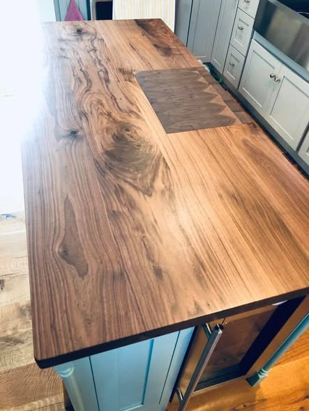 Angled view of the installed walnut island top showing the end-grain cutting board inlay, painted island base, and brushed stainless appliances behind.