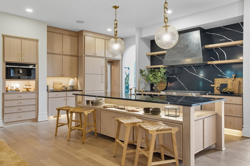 Light rift-sawn white oak kitchen with floor-to-ceiling cabinetry, integrated appliance niches, custom hood, and a long island with black stone waterfall top
