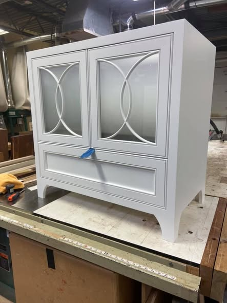 Two-door extra-white vanity cabinet with curved overlapping radius mullions framing frosted glass, large flat drawer below, hand-shaped cabriole feet, and conversion-varnish finish