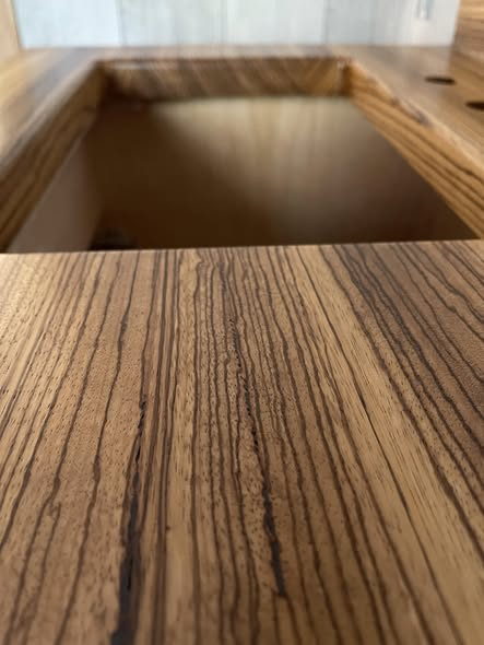 Close-up grain detail of the Zebrano top showing alternating cream and dark chocolate stripes around the sink opening